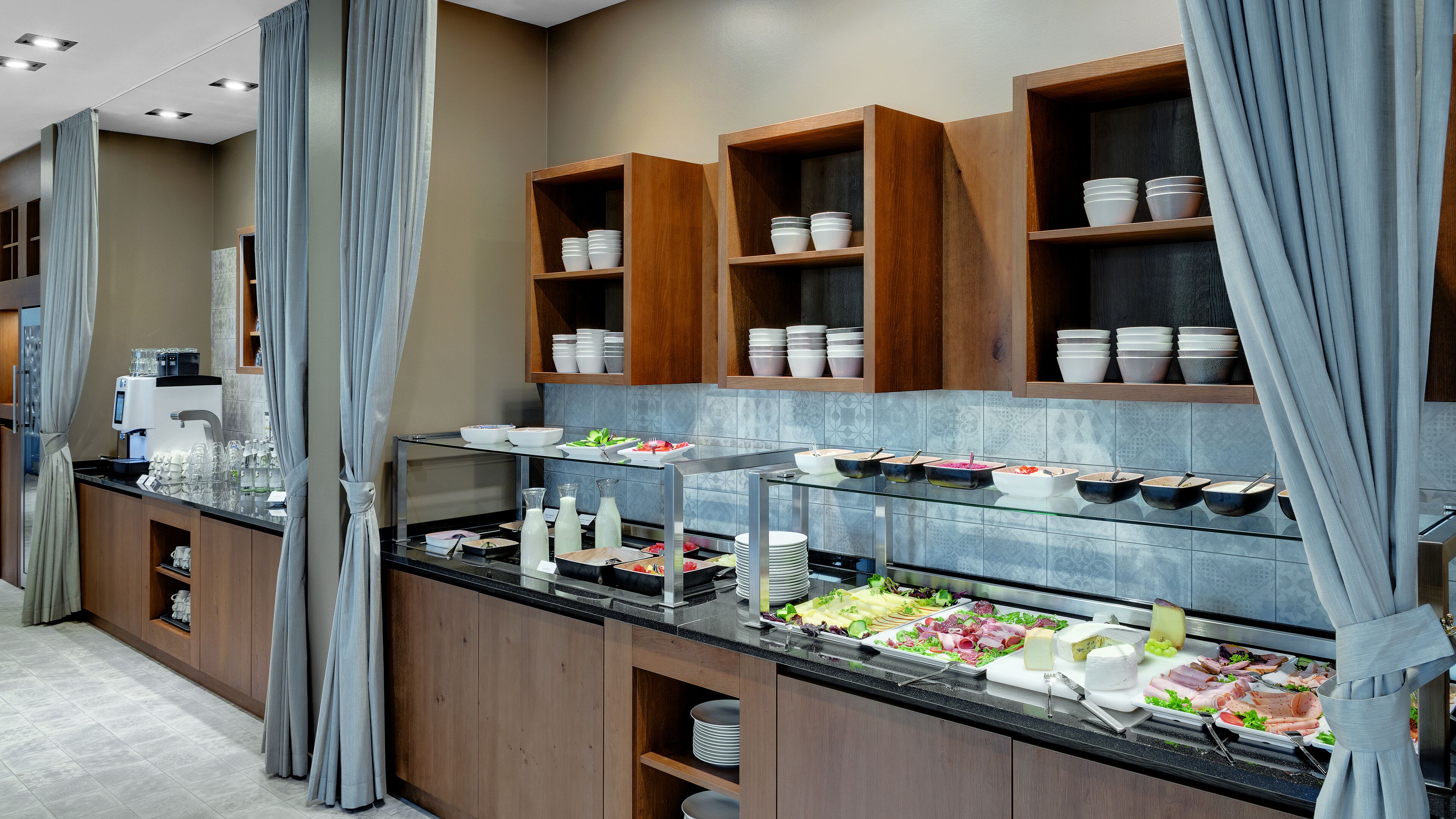 Disposição de buffet com diversos alimentos, uma máquina de café e uma vitrine de vidro.