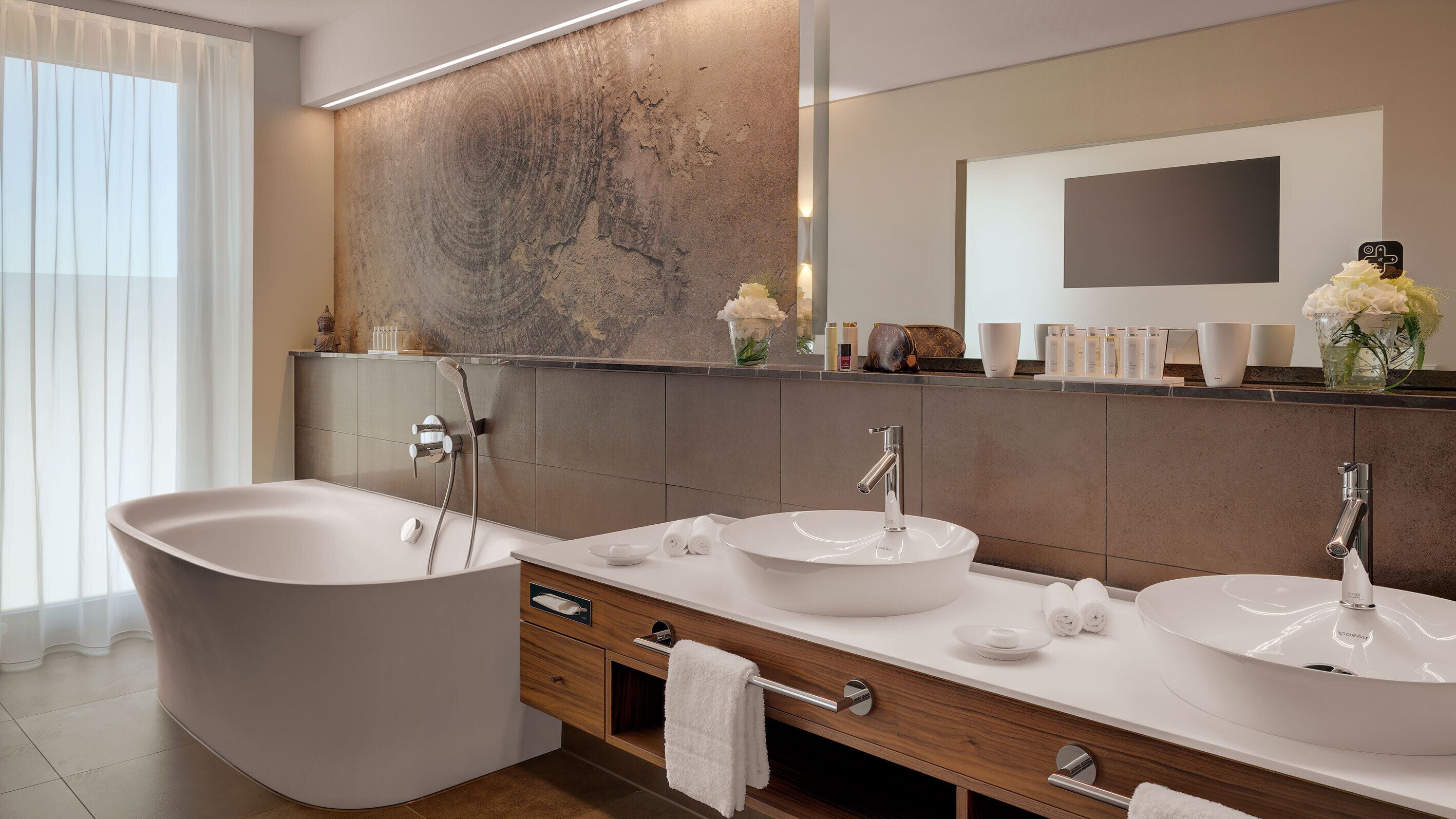 A modern bathroom with a freestanding bathtub, two sinks, a vanity with drawers, and a large mirror.