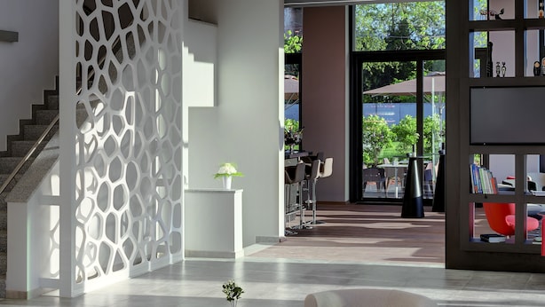 A modern interior with a staircase, a decorative white partition, a round chandelier, and seating areas.