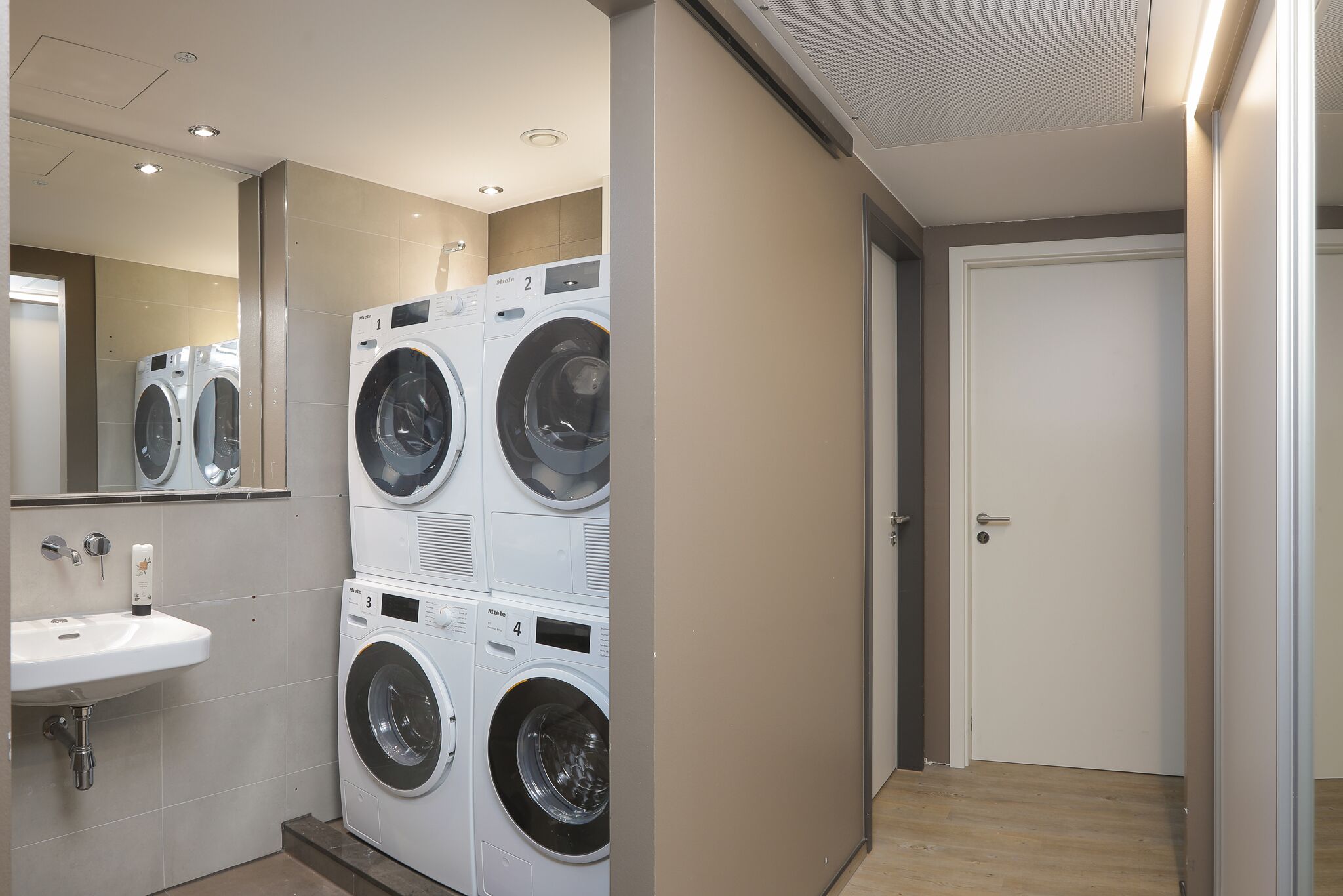 Un cuarto de lavandería con cuatro lavadoras apiladas, un lavabo y un espejo.
