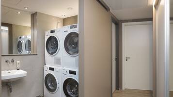 Un cuarto de lavandería con cuatro lavadoras apiladas, un lavabo y un espejo.