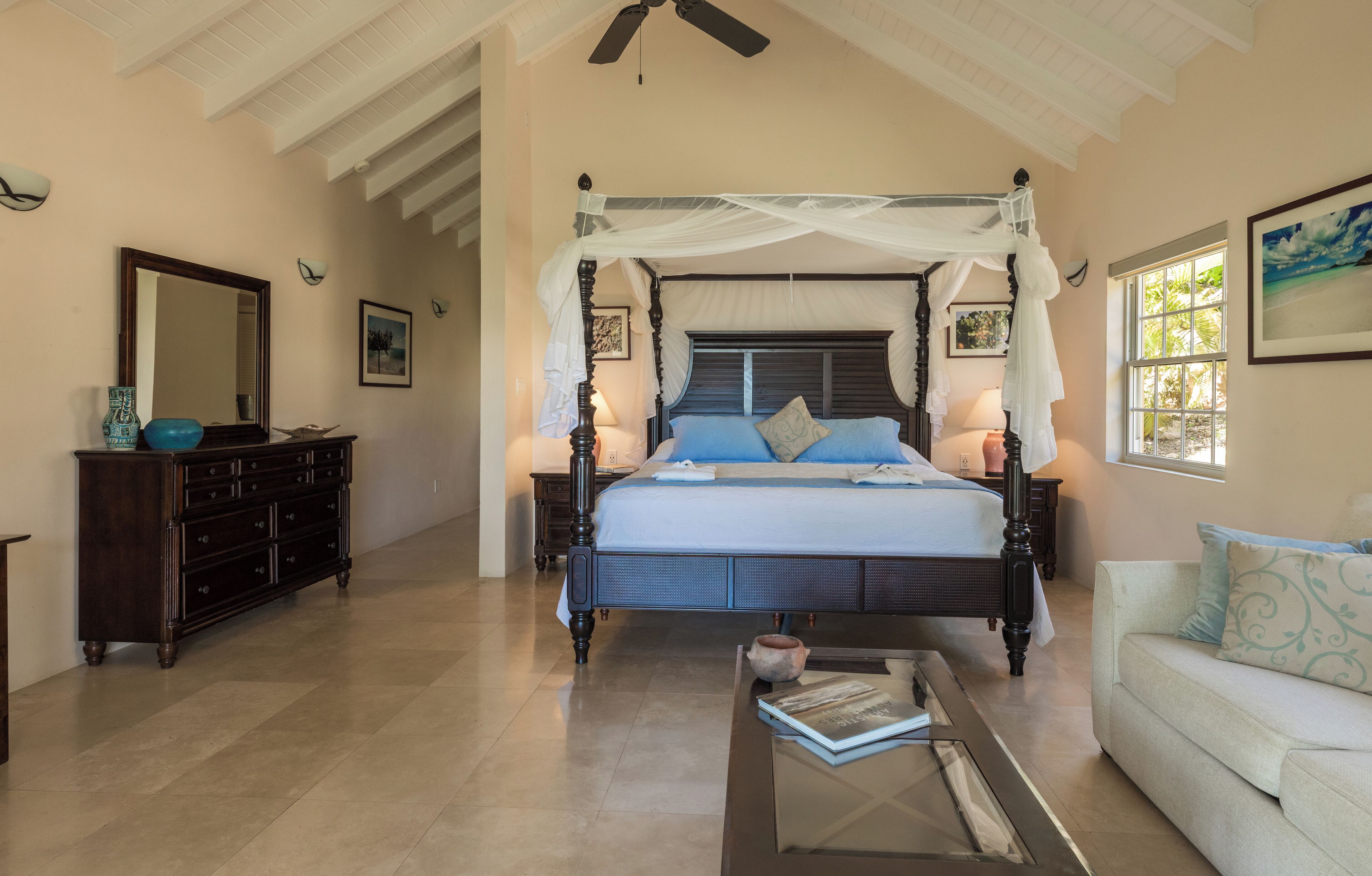 A spacious bedroom with a four-poster bed, a nightstand, a dresser, and a window with a view.