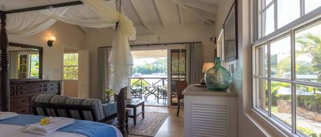 A bedroom with a large bed, a nightstand, a chair, a table, and a view of the outdoors through a window.