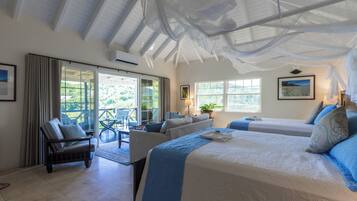 Habitación de hotel con una cama grande, un sofá y una silla. Tiene un balcón con vistas al entorno verde.