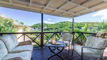 Un espace extérieur aménagé, abrité et doté d'une table pour deux, entouré de meubles en osier et offrant une vue sur un paysage verdoyant luxuriant.