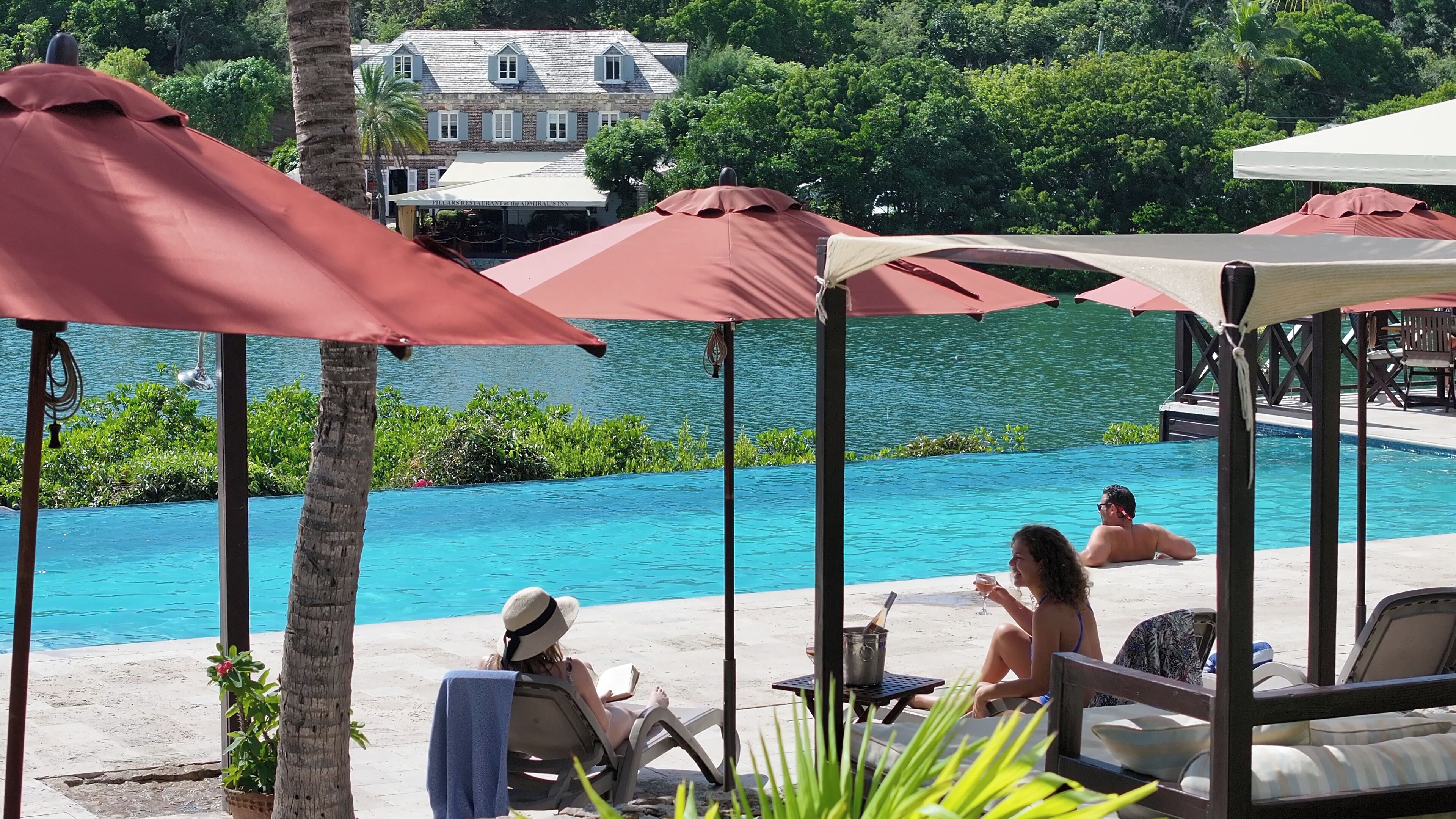 Zona junto a la piscina con sillas de descanso, sombrillas y vistas a un lago.