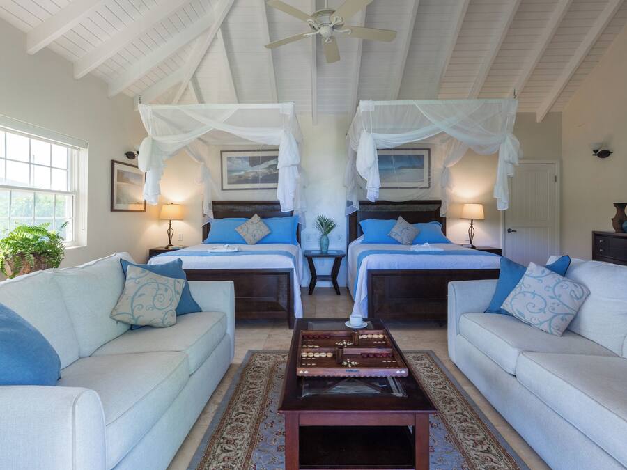 A hotel room with two beds, a sofa, a coffee table, and a ceiling fan.