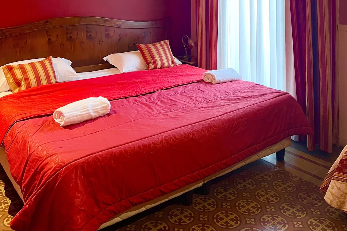 A hotel room with a large bed, red walls, and striped curtains.