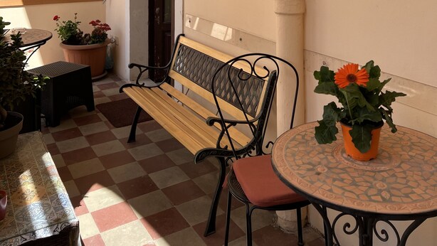 A small outdoor seating area with a bench and a table, surrounded by potted plants and a tiled floor. - Hotel Valentino (Catania)