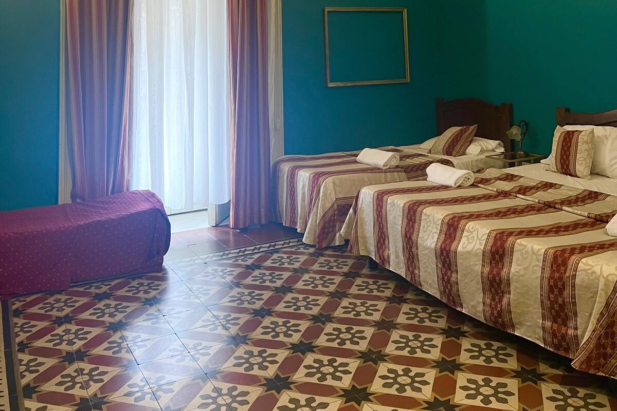 A hotel room with two beds, a window with curtains, a patterned floor, and a framed picture on the wall.