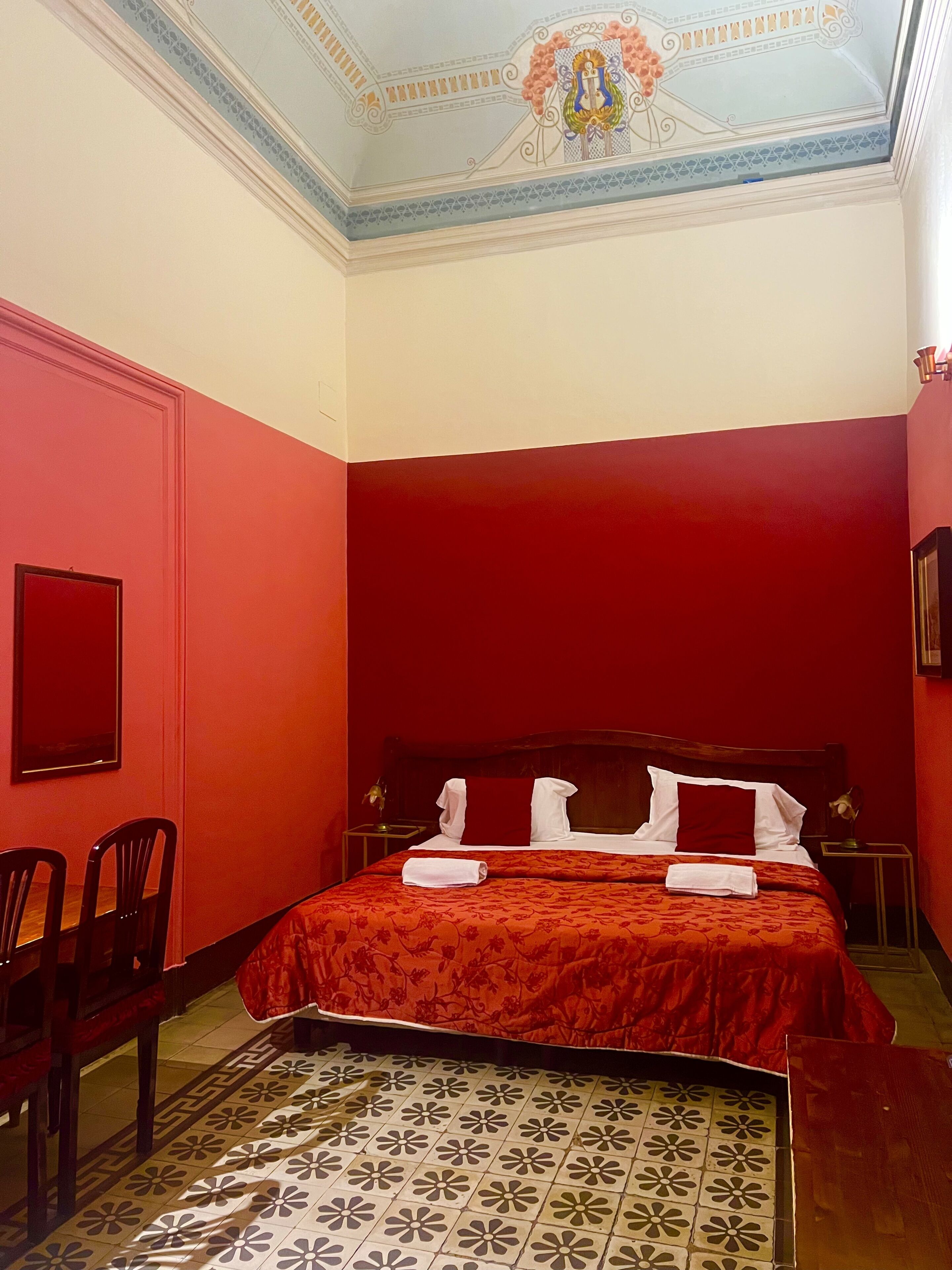A hotel room with a red and white color scheme, a bed with white linens, a wooden headboard, and a decorative ceiling.