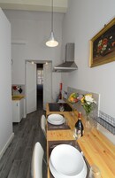 Un'area pranzo con un tavolo di legno apparecchiato per due persone, un quadro al muro e una cucina sullo sfondo.