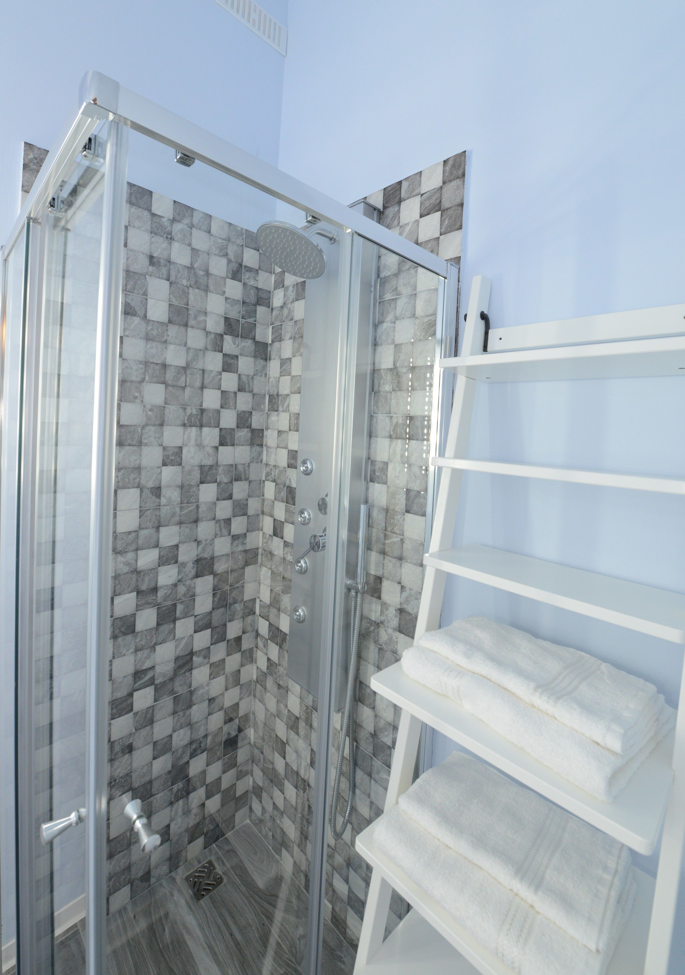 A glass-enclosed shower with checkered tile walls, a white towel rack, and a metal drain.