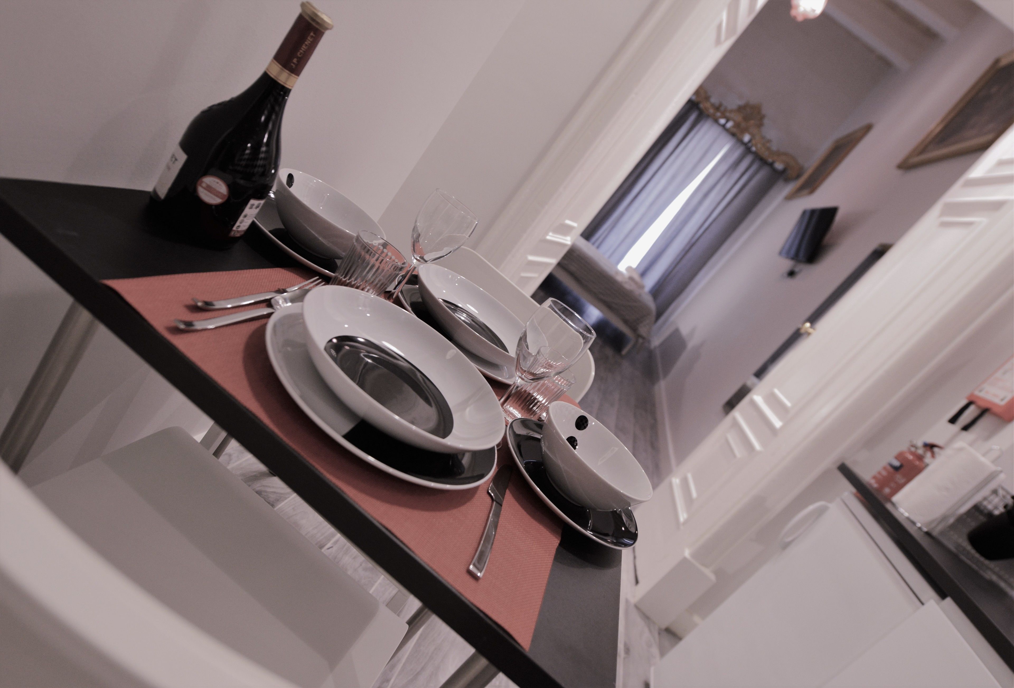 A dining table set with plates, cutlery, and a bottle of wine.