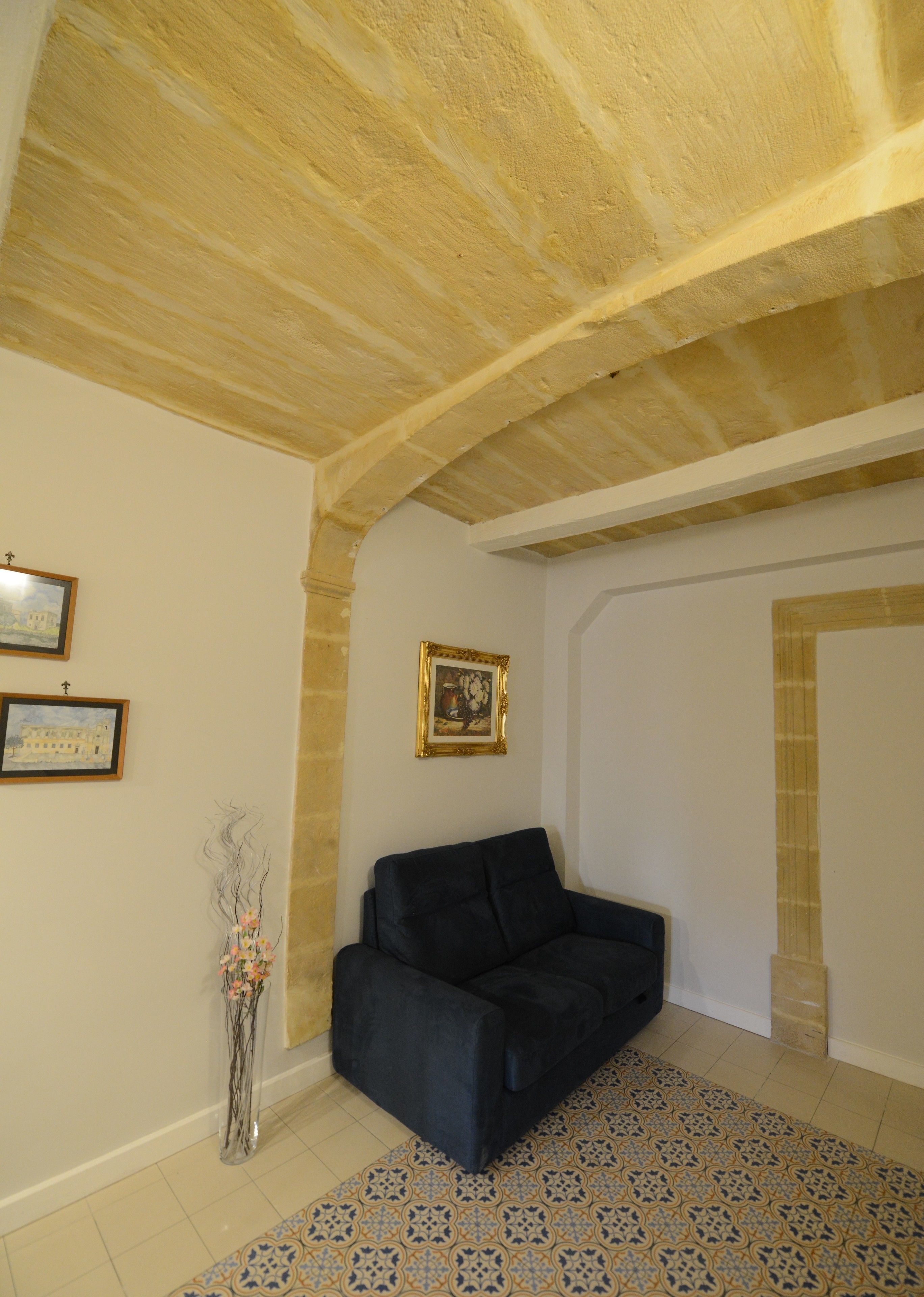 A room with a dark sofa, a tiled floor, and a wooden ceiling.