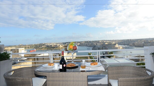 A balcony with wicker furniture, a bottle of wine, and a fruit bowl.