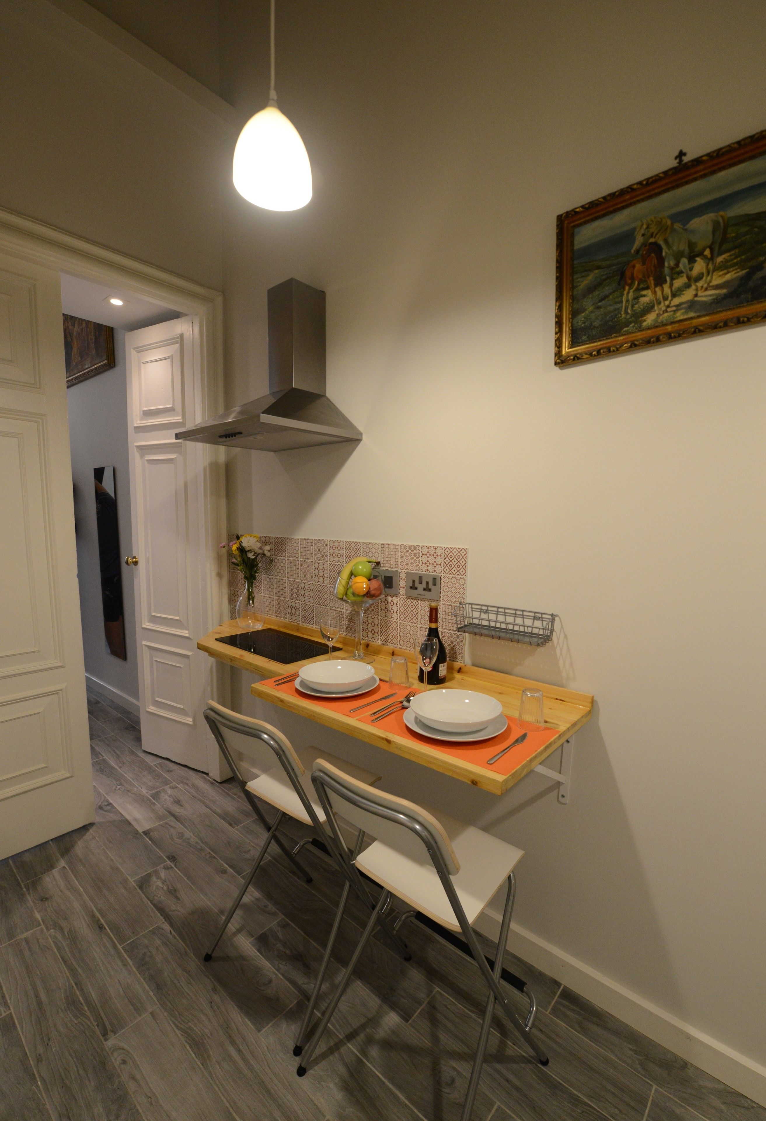 A compact kitchen with a dining area, including a sink, a stove hood, and a painting on the wall.