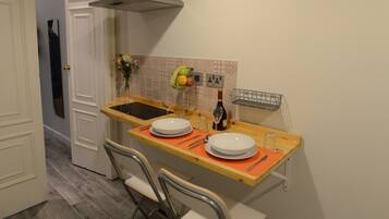 A compact kitchen with a dining area, including a sink, a stove hood, and a painting on the wall.