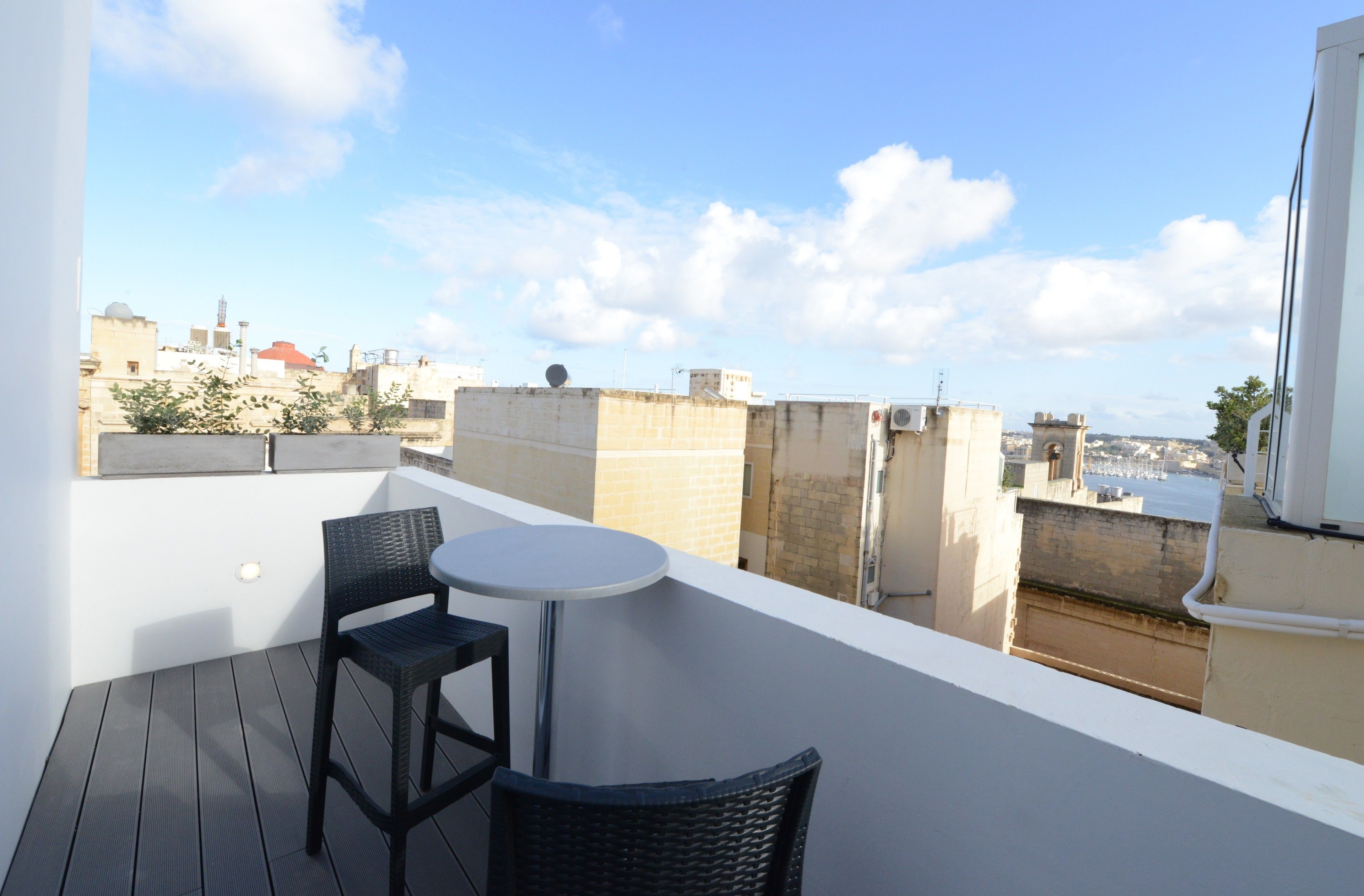 Un balcón con una mesa redonda y dos sillas, con vistas a un paisaje urbano con edificios y cielo despejado.