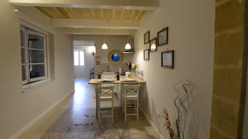 A narrow hallway with a tiled floor leading to a kitchen area with a dining table and chairs.