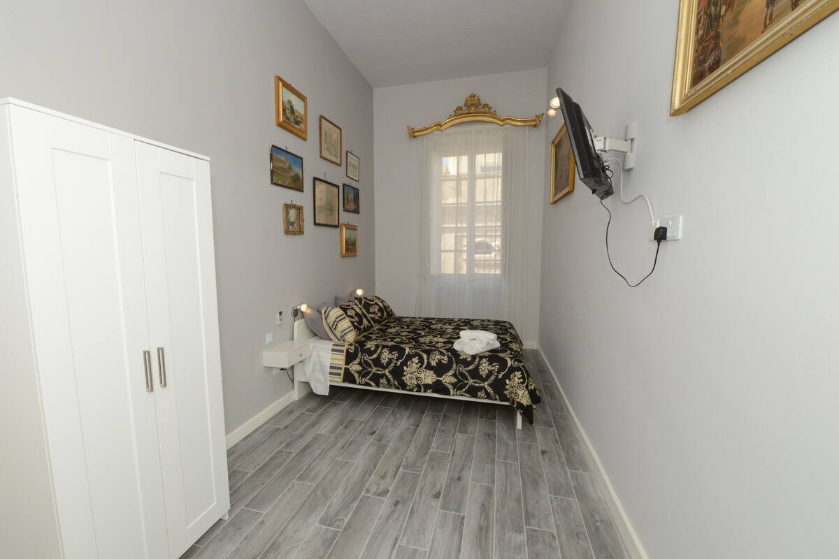 A bedroom with a bed, a wardrobe, a window with curtains, and wall-mounted artwork.
