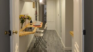 A narrow hallway with a wooden table set for dining, a chair, and a wine bottle.