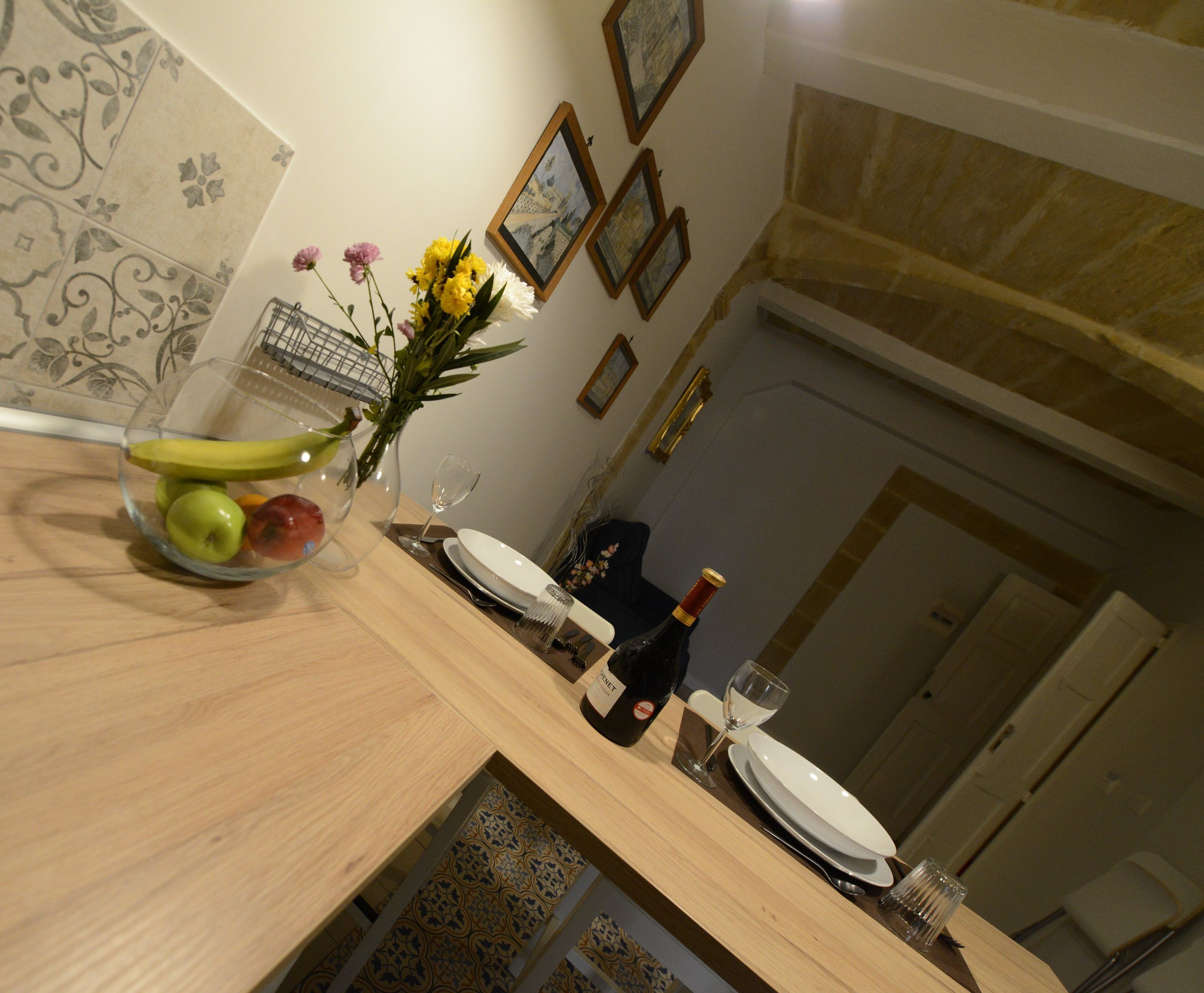 A dining area with a wooden table set for two, a vase with flowers, and framed pictures on the wall.