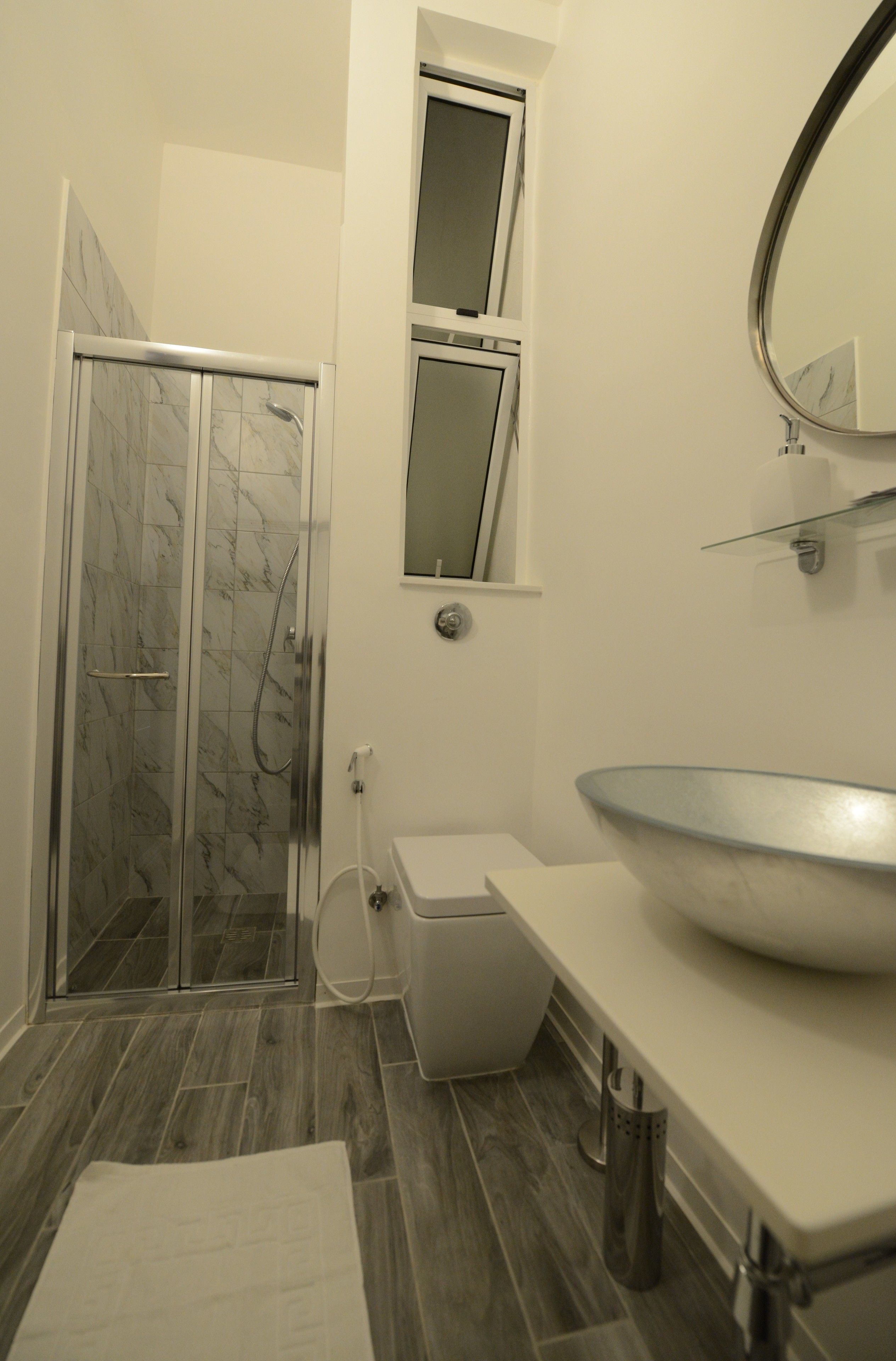 Un baño con ducha envuelta en vidrio, inodoro blanco, lavamanos grande con cuenco y espejo sobre el lavamanos.