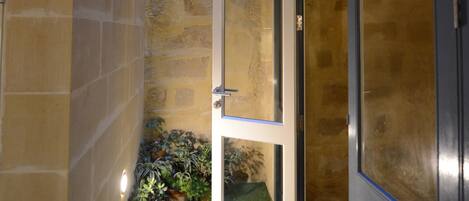 A narrow hallway with a door, potted plants, and a textured wall.