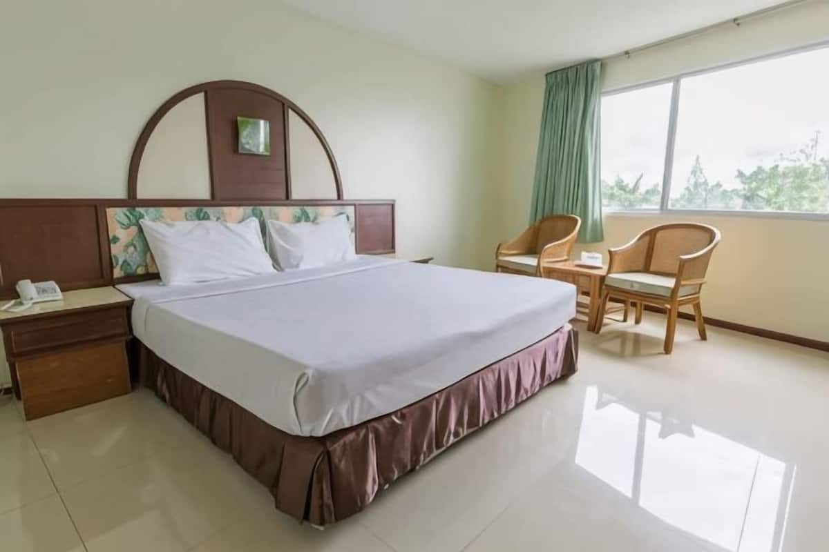 A hotel room with a large bed, a nightstand, a desk with a chair, and a view of the outdoors.