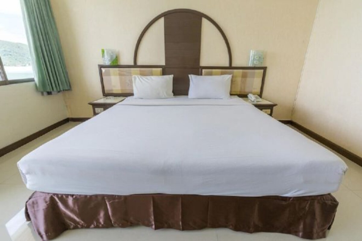 A neatly made bed with a headboard, a bedside table with a lamp, and a window with curtains.