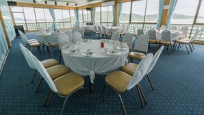 A conference room with round tables and chairs, large windows with curtains, and a view of the outdoors. - Lake Inn Hotel (Songkhla)
