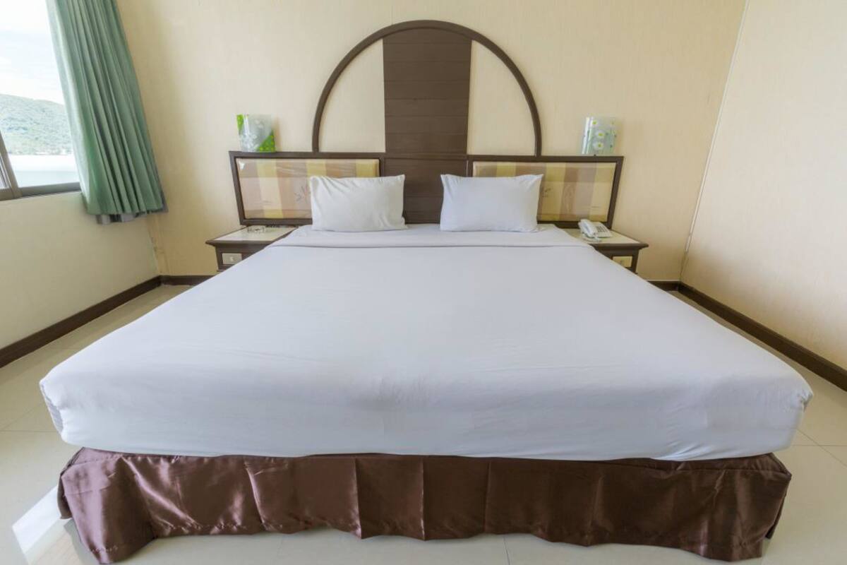 A neatly made bed with a brown skirt, a headboard with a mirror, and two bedside tables with lamps.