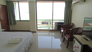 A hotel room with a bed, a TV, a desk, and a chair. There are curtains on the windows and an air conditioning unit on the wall. - Lake Inn Hotel (Songkhla)