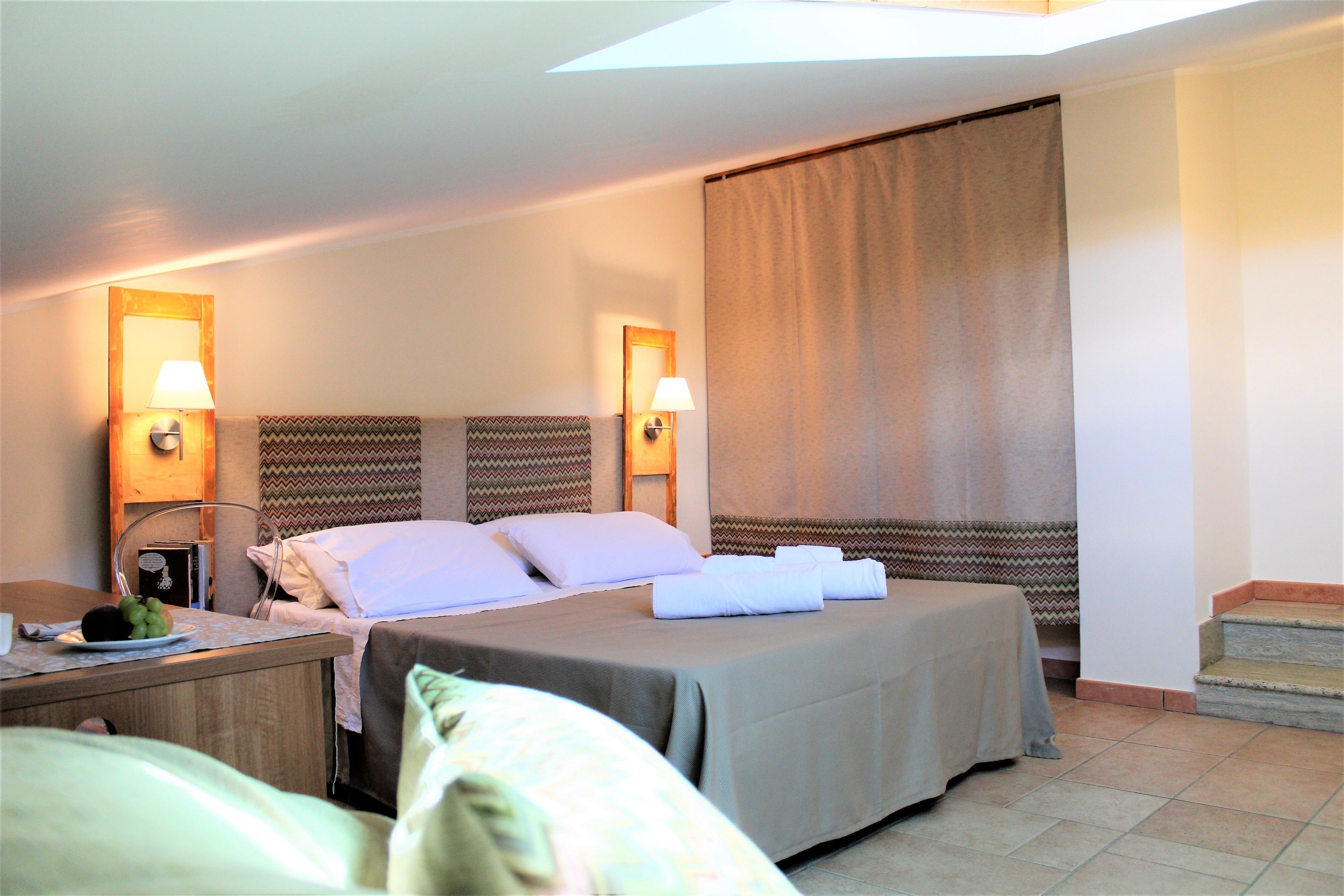 Habitación de hotel con cama, lámparas de noche, mesita de noche con lámpara y ventana con cortinas.