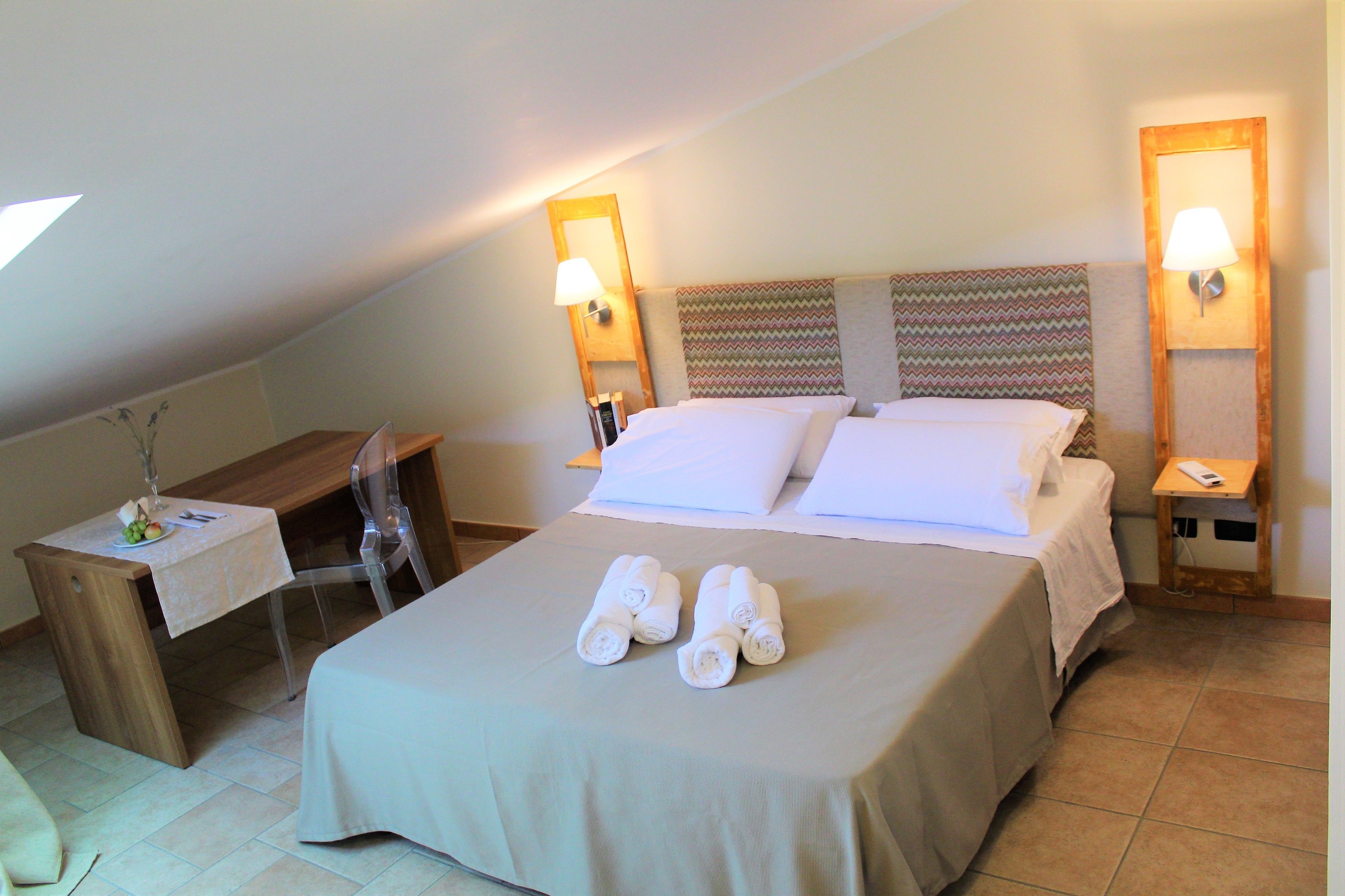 A hotel room with a bed, two bedside tables, a desk, and a chair.