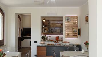 Una cocina moderna con una isla central, un área de comedor con sillas traslúcidas y una barra con estantes y una lámpara colgante.