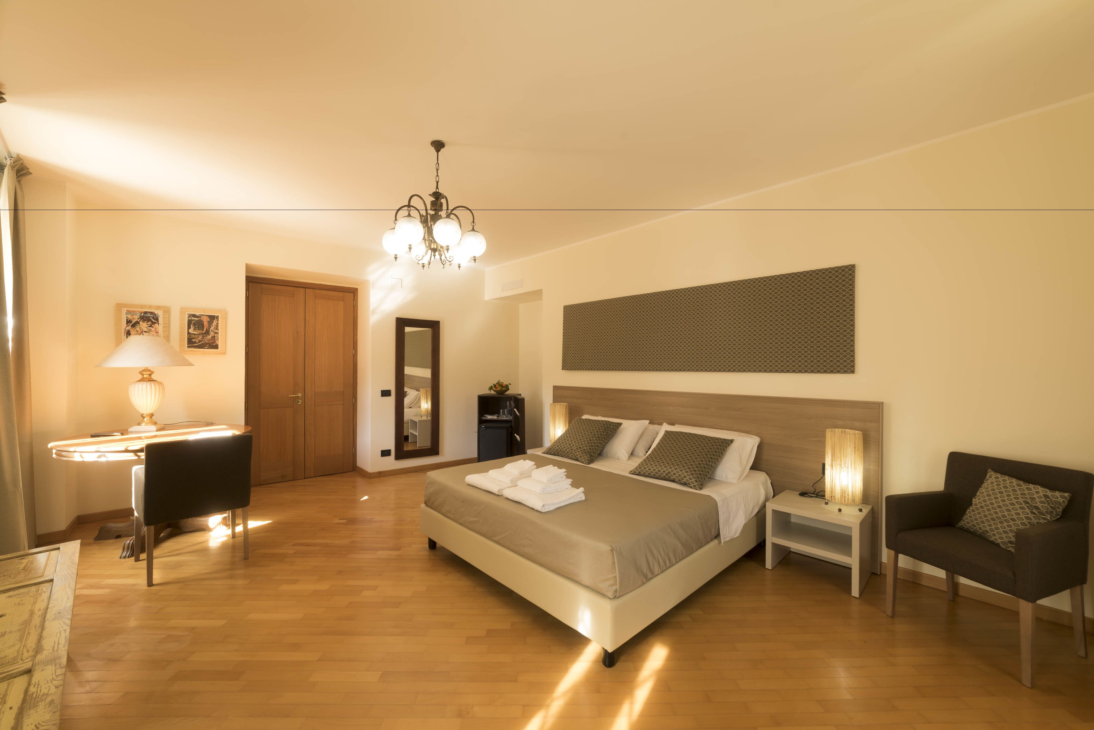 A modern bedroom with a large bed, bedside tables, a chair, a desk, and a chandelier.