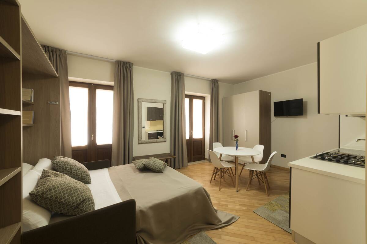 A hotel room with a bed, a desk, a chair, a TV, and a dining table.