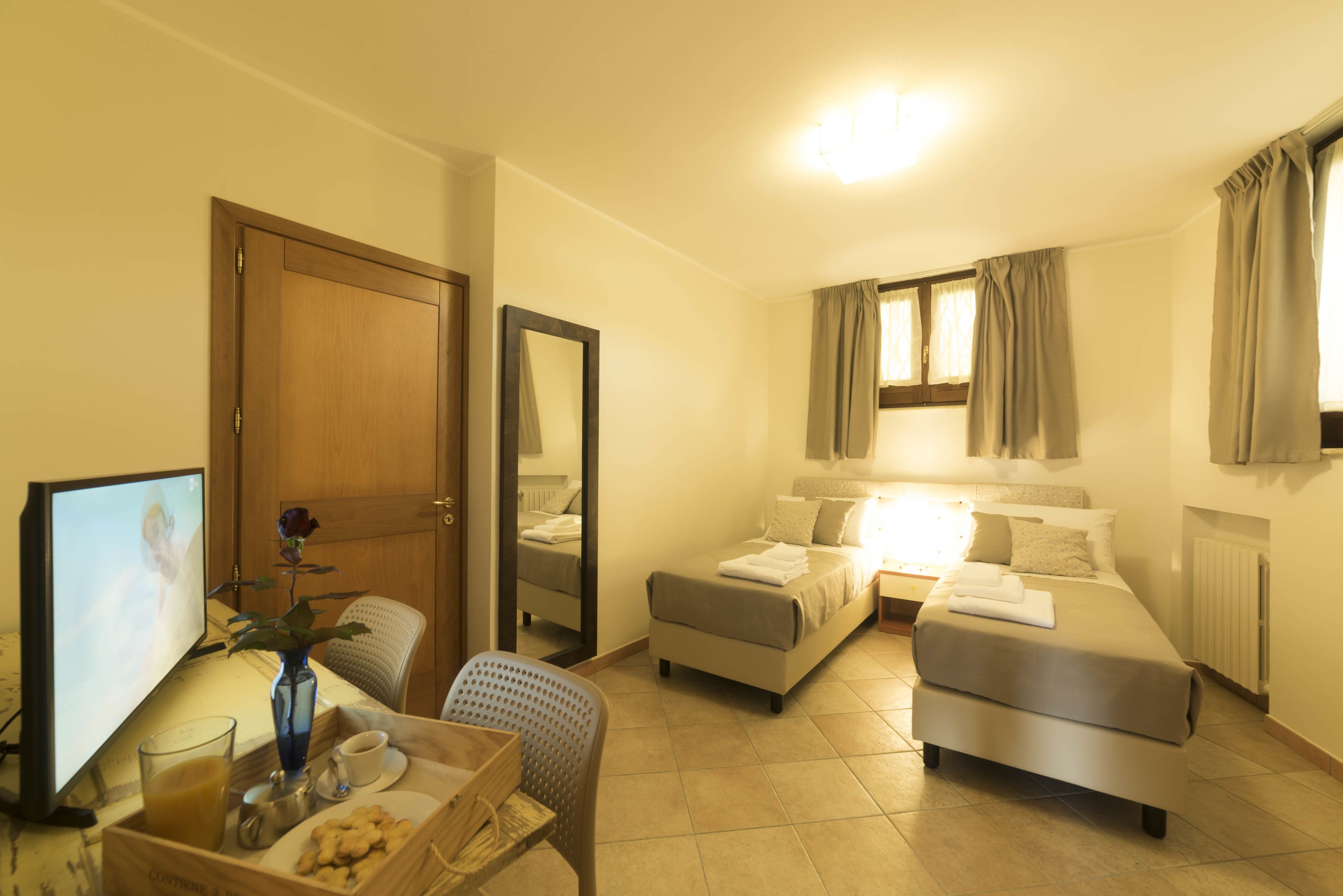 A hotel room with a bed, a sofa, a TV, a coffee table with a vase and cookies, and a window with curtains.