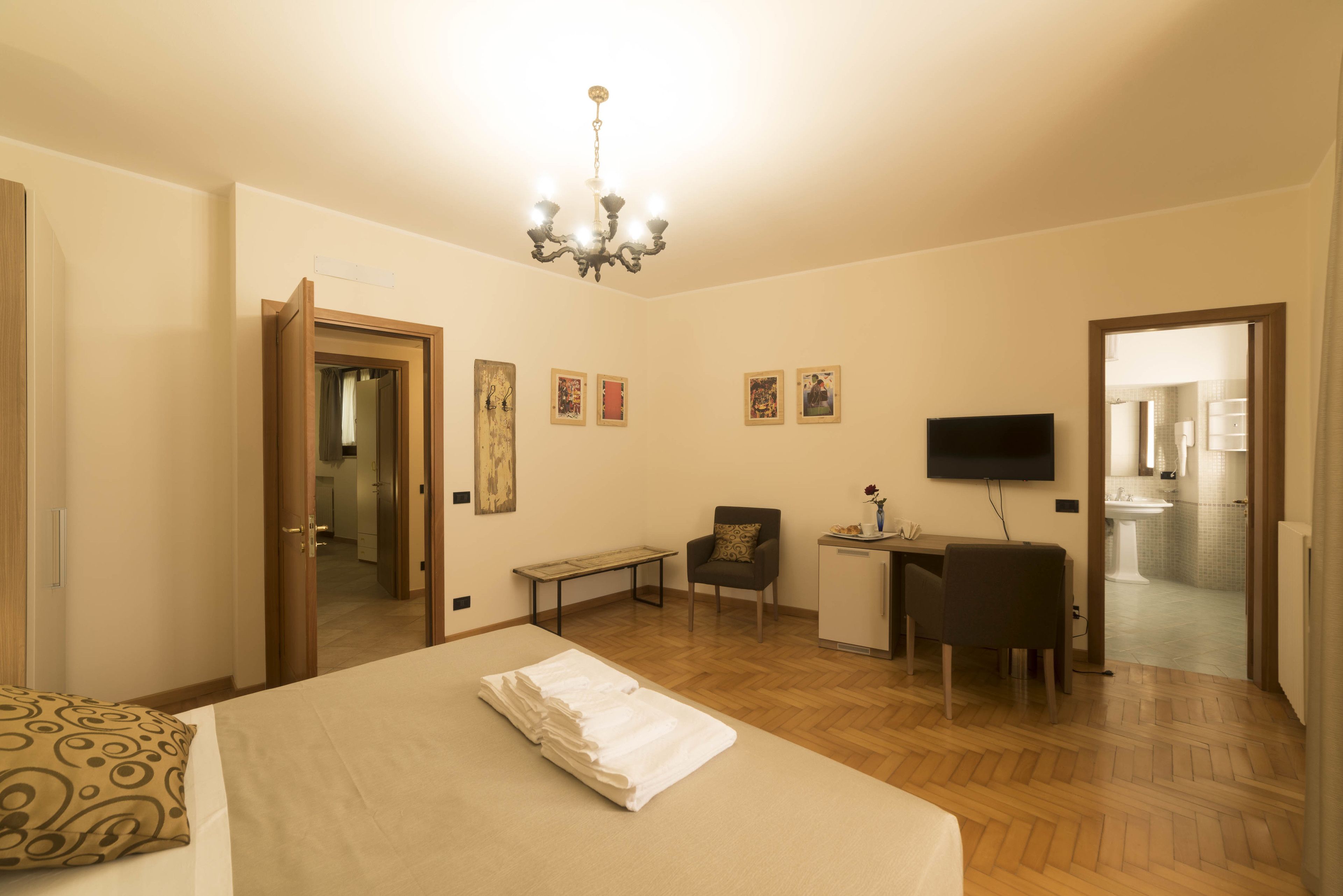 A hotel room with a bed, a desk, a chair, a television, and a bathroom visible through an open door.