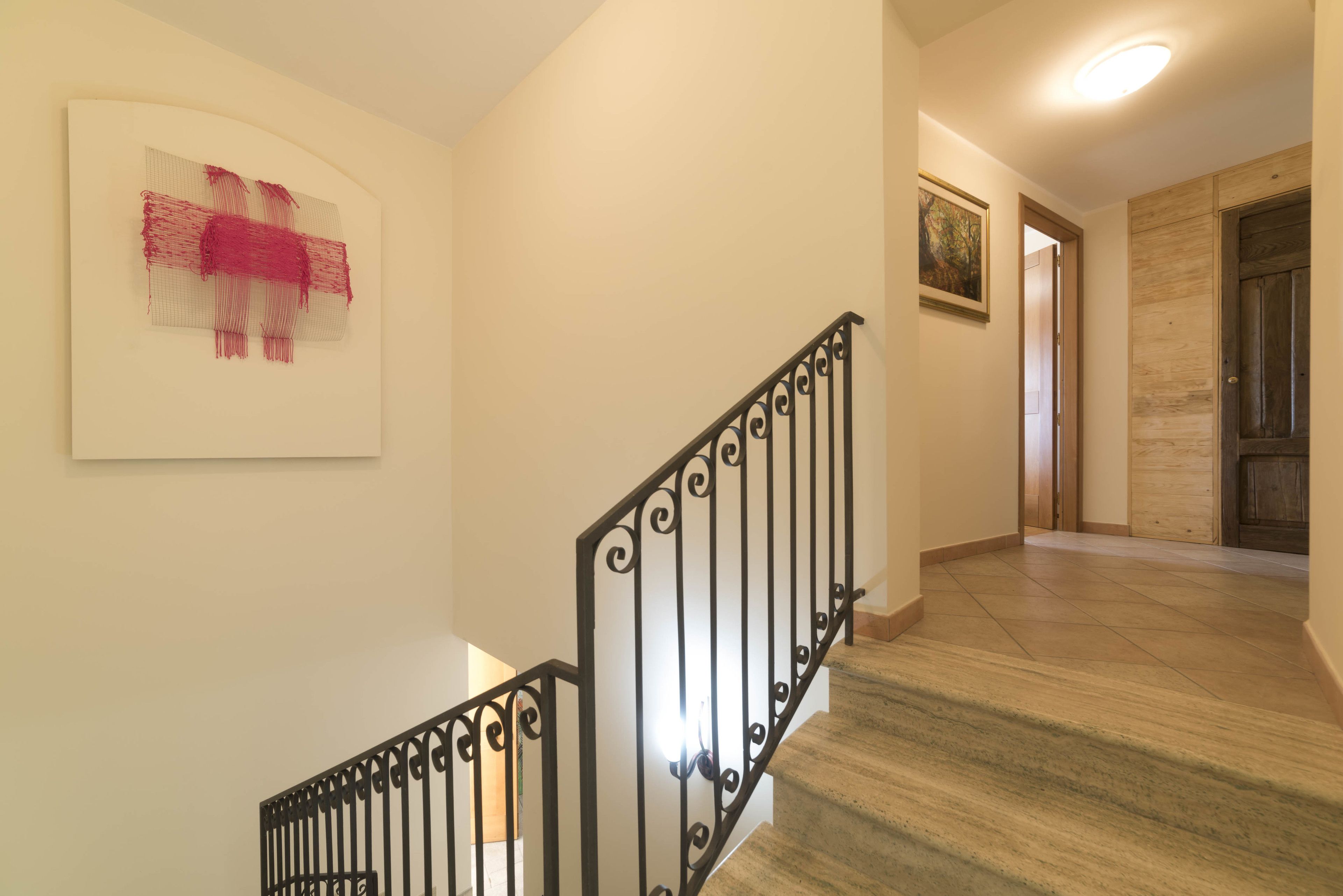 Una escalera con barandilla negra, una obra de arte enmarcada en la pared y una puerta de madera al fondo.