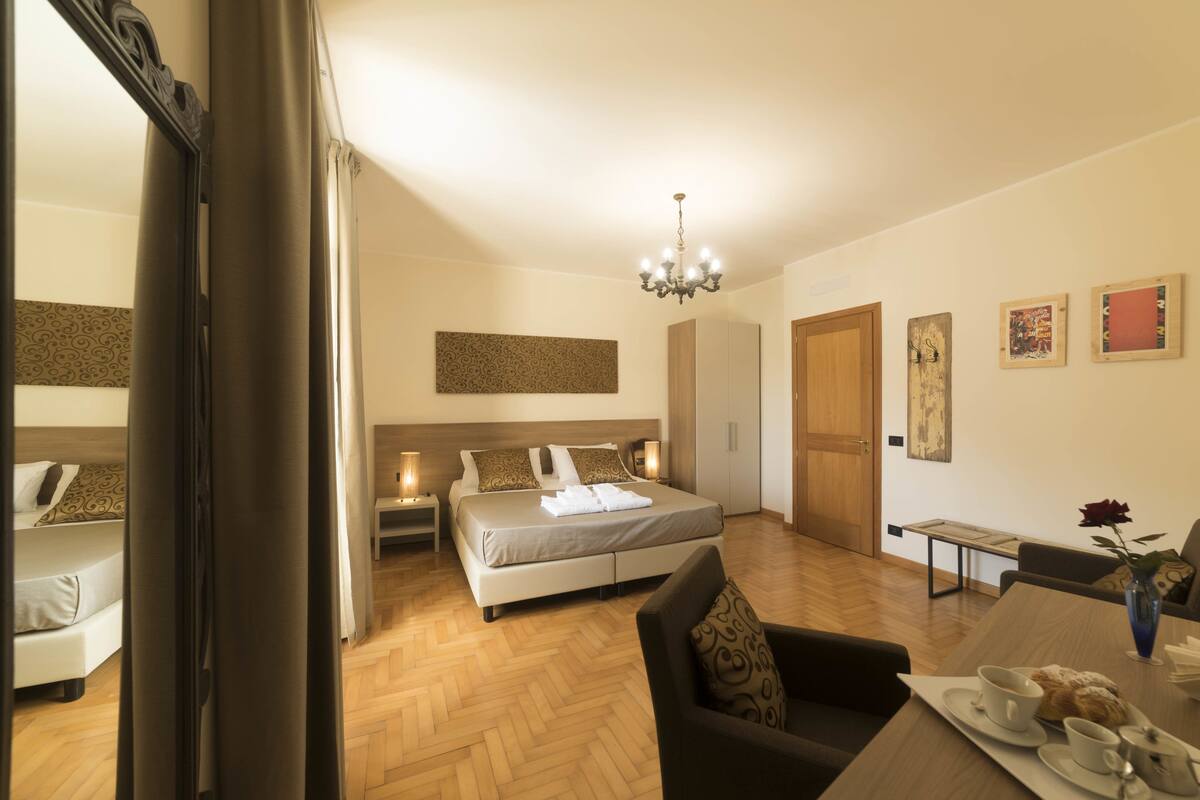 A hotel room with a bed, bedside tables, a dining table with a vase of flowers, and a chair.