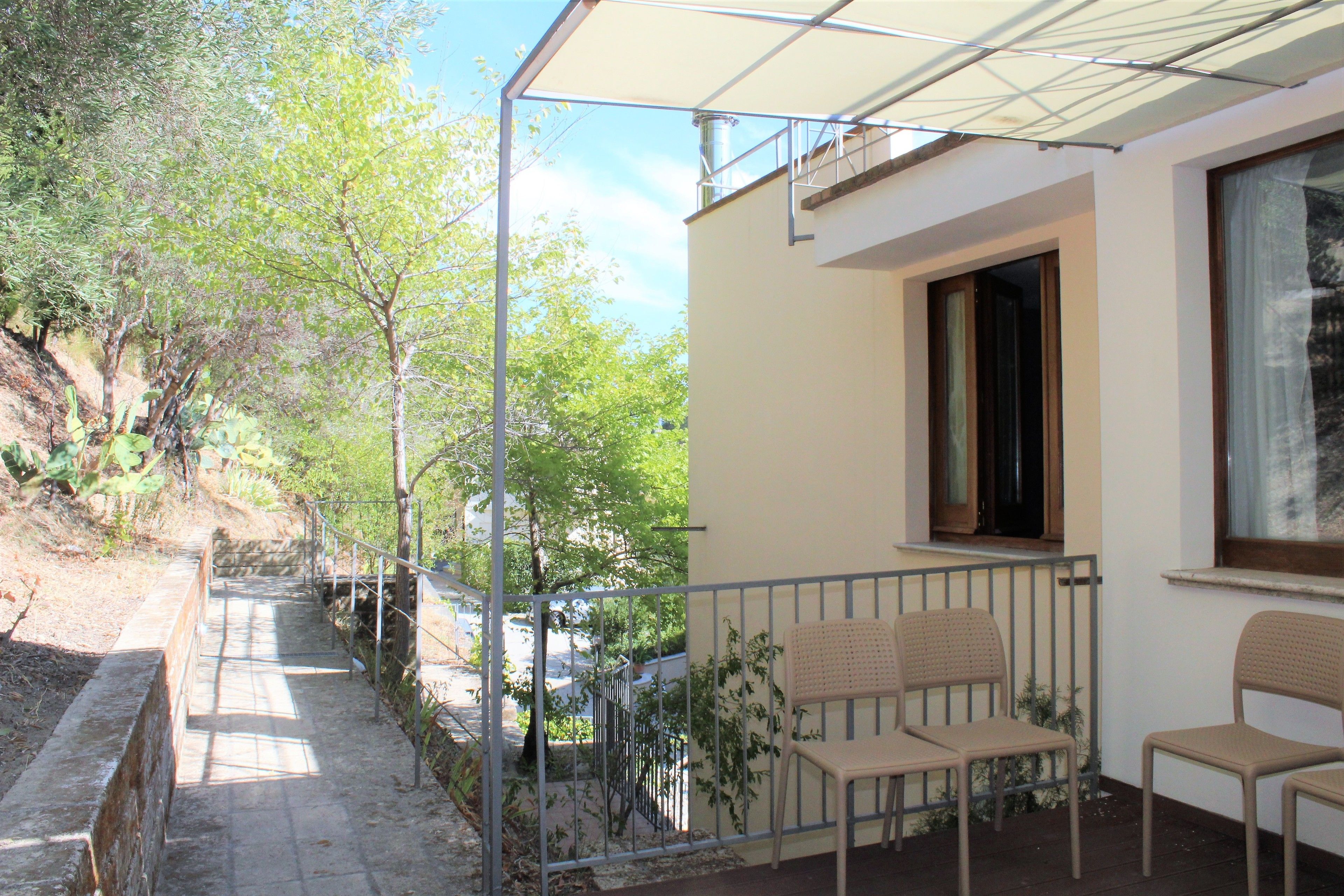 Un balcon avec deux chaises, une fenêtre et une vue sur des arbres et une route.