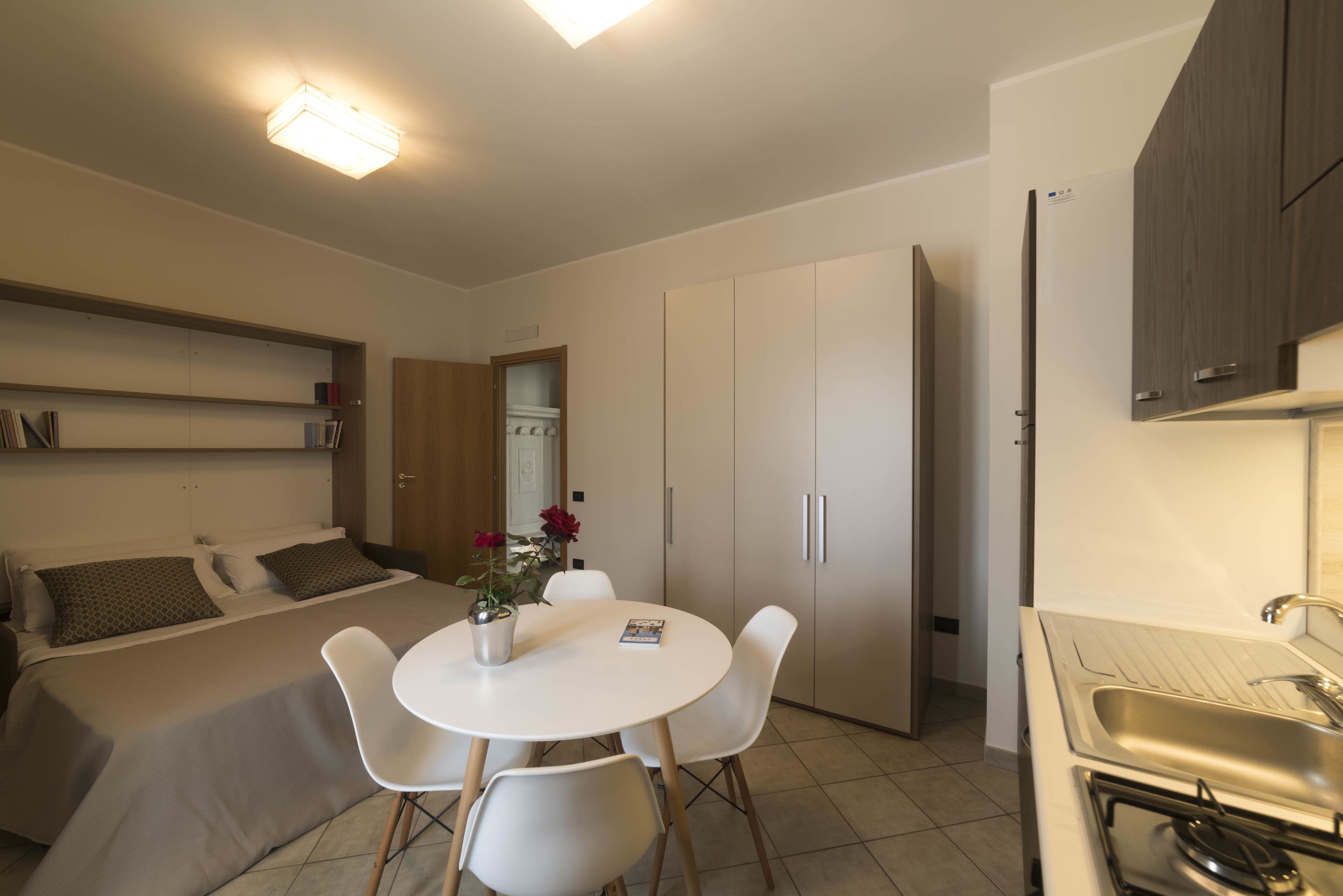 Une chambre d’hôtel de taille réduite comprenant un lit, une petite table à manger avec des chaises, un coin cuisine et une salle de bain.