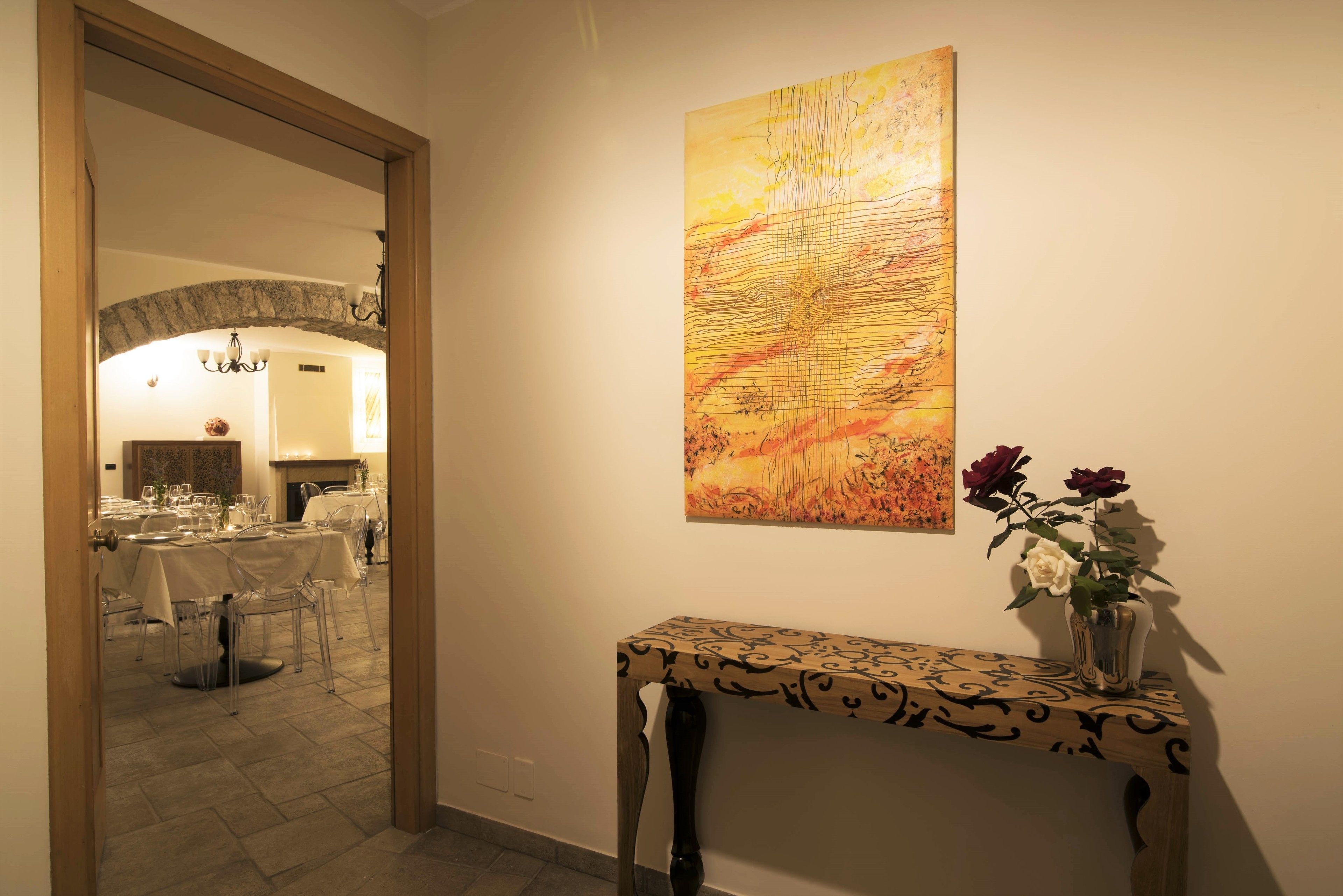 Un coin repas avec des tables dressées pour le repas, une grande peinture abstraite au mur et un vase rempli de fleurs sur une console.