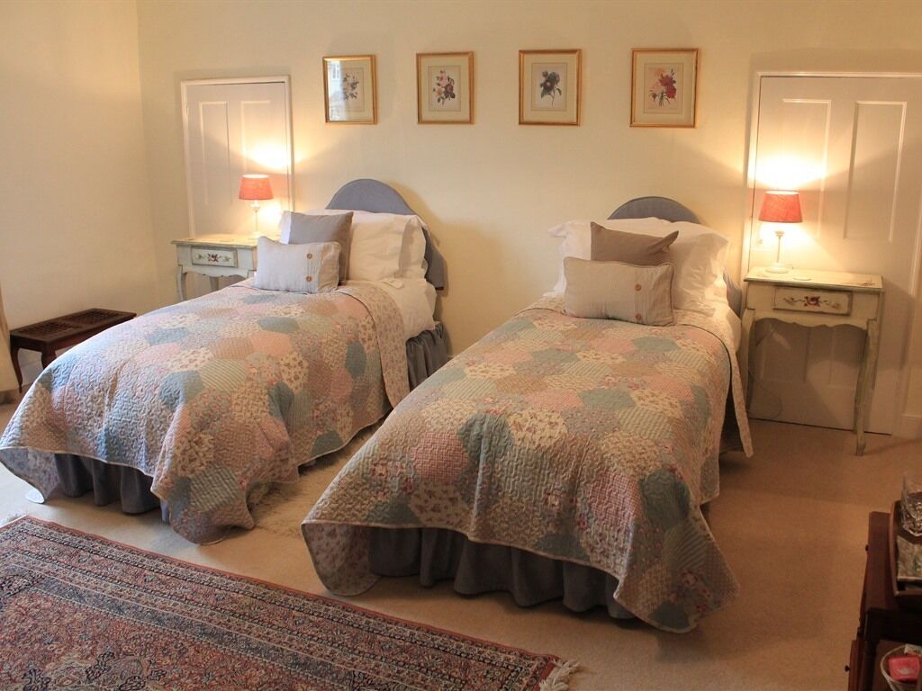 A bedroom with two beds, each with a matching headboard and footboard, flanked by bedside tables with lamps.