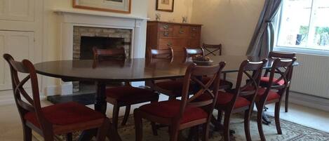 Un comedor con una mesa redonda y sillas de madera, una chimenea y un ventanal con cortinas.