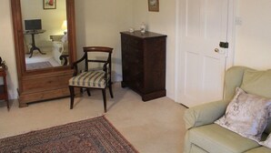 Une pièce avec un grand miroir, une commode en bois, une chaise, un canapé vert et un tapis à motifs.