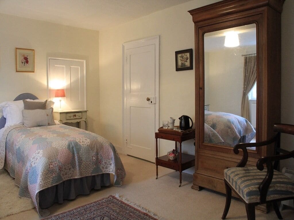 Une chambre à coucher comprenant un lit, une table de chevet, une lampe, une commode, une chaise et un miroir.